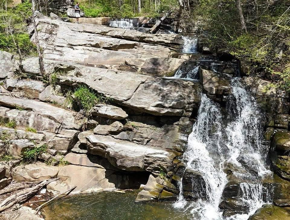 Water cascades over broad rock ledges in a wooded setting.